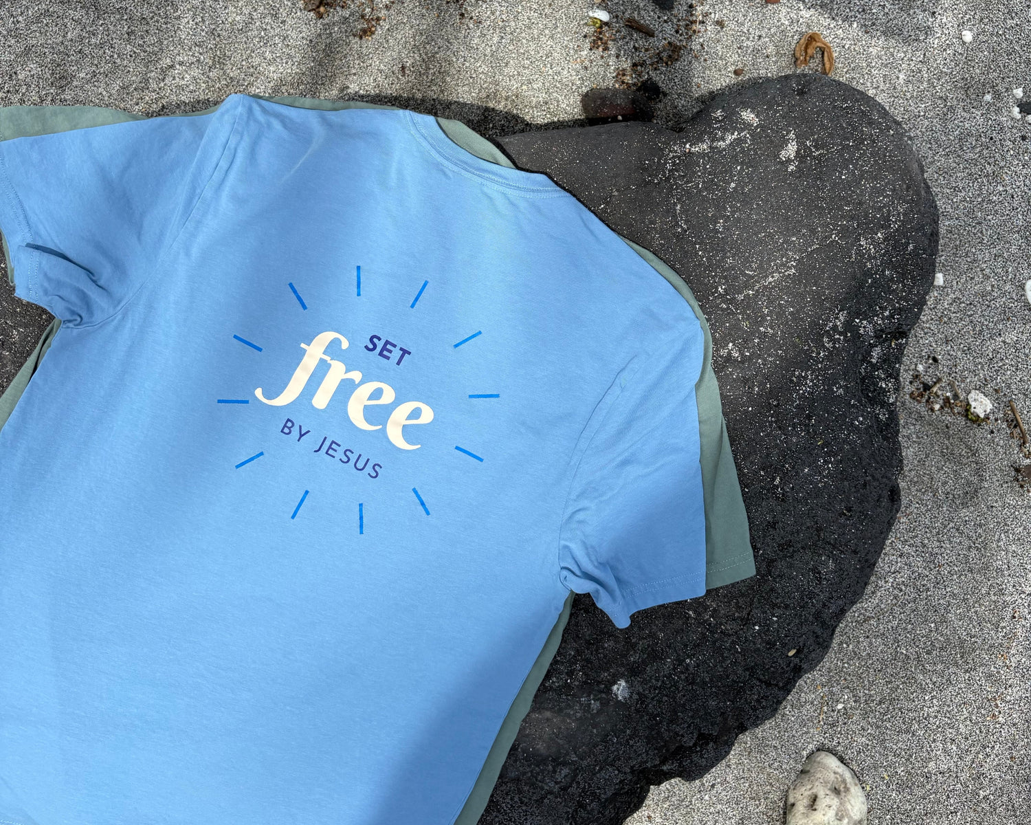 Blue t-shirt with 'Set Free by Jesus' text on a rock at the beach