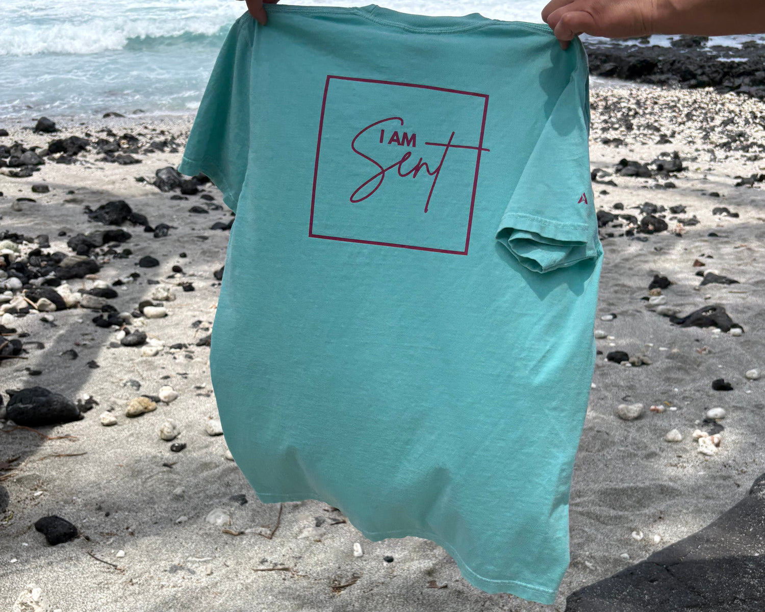 Person holding a turquoise bag with a logo on a beach